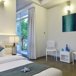 Guest room at Velana Beach Hotel Maldives with a double bed, two chairs and a balcony door